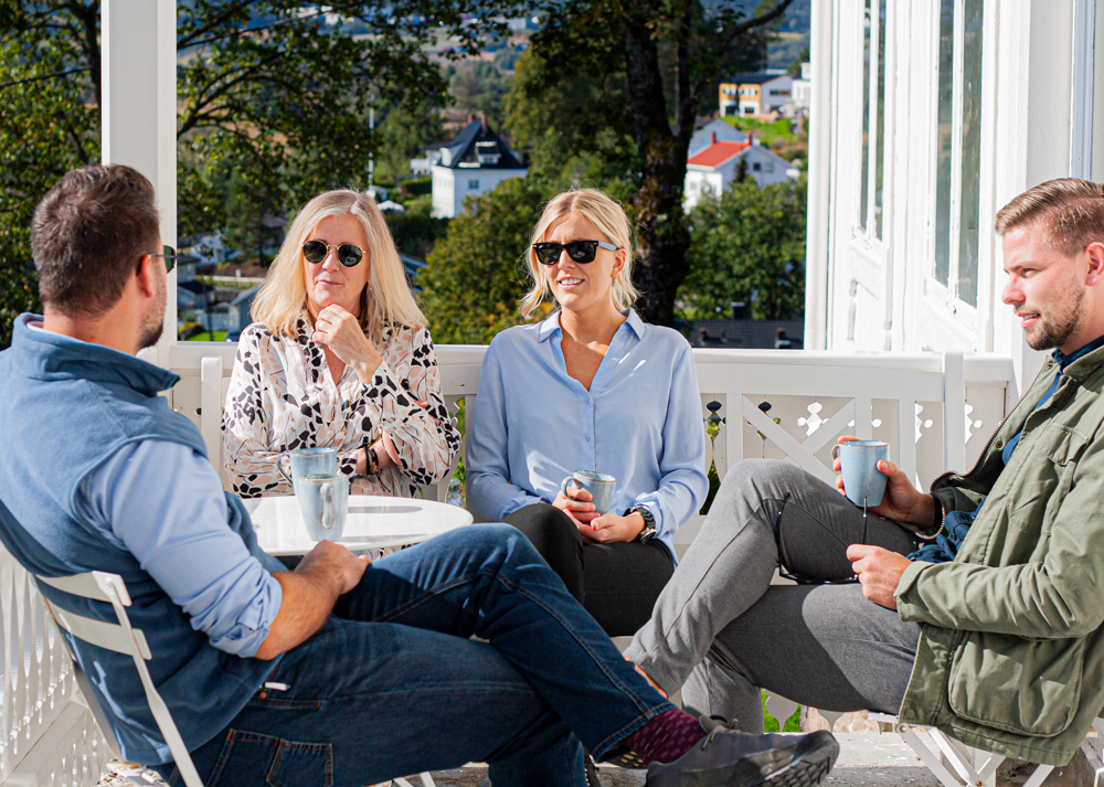 Fire personer koser seg i solskinn på verandaen på Kjeller Gaard